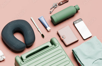 Collection of travel items including a neck pillow, water bottle, wallet, and suitcase on a pink background